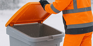 Person in oranger Arbeitskleidung öffnet Tonne während es schneit